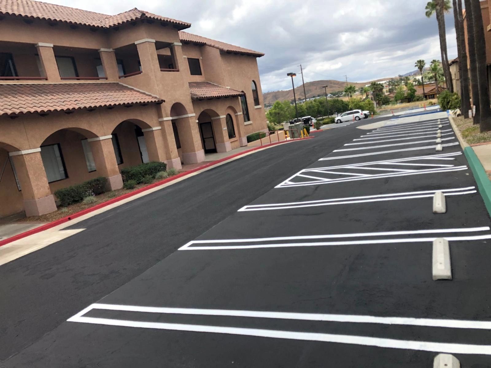 Empty parking lot with freshly painted white lines beside a building under cloudy sky.
