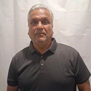 Man with gray hair wearing a black polo shirt against a plain backdrop.