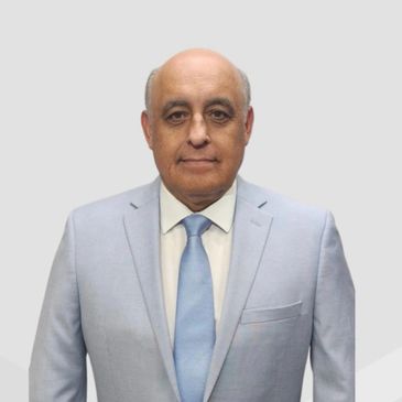 Man in light blue suit and tie posing against a plain background.