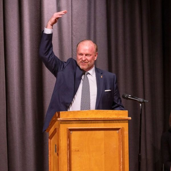 Man in suit gestures while speaking at podium with microphone.