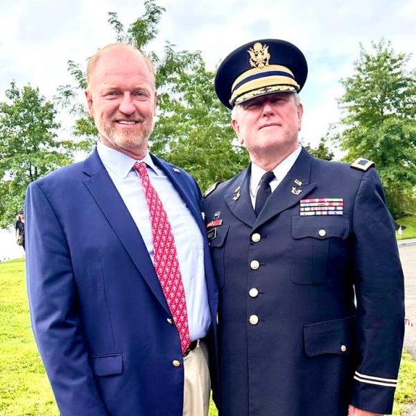 Two men posing outdoors, one in a suit and the other in a military uniform.