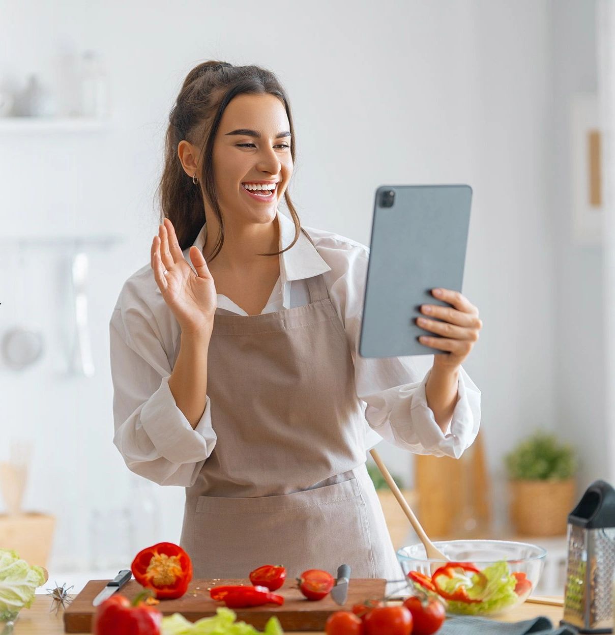 Young woman video chatting in the kitchen while preparing a meal.
