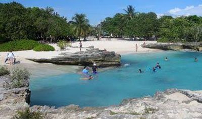 People swimming and relaxing at a beach with clear blue water.