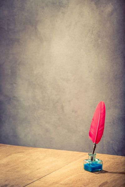 Vintage old red quill pen with inkwell on wooden table front concrete wall background. 