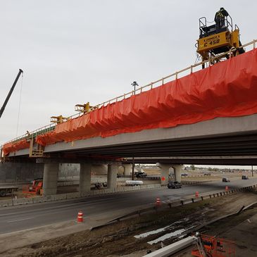 Construction workers operating machinery on a bridge over a highway.