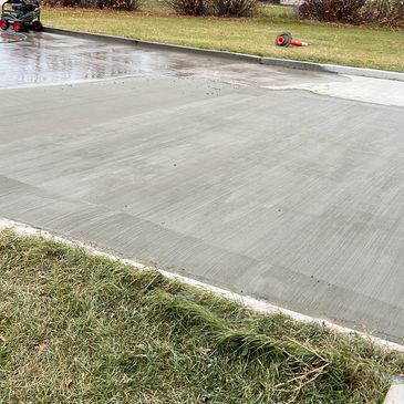 Newly poured concrete sidewalk beside green grass and garden beds.