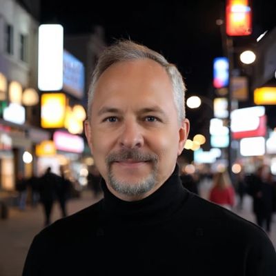 Man with gray hair and beard smiling in a city at night.
