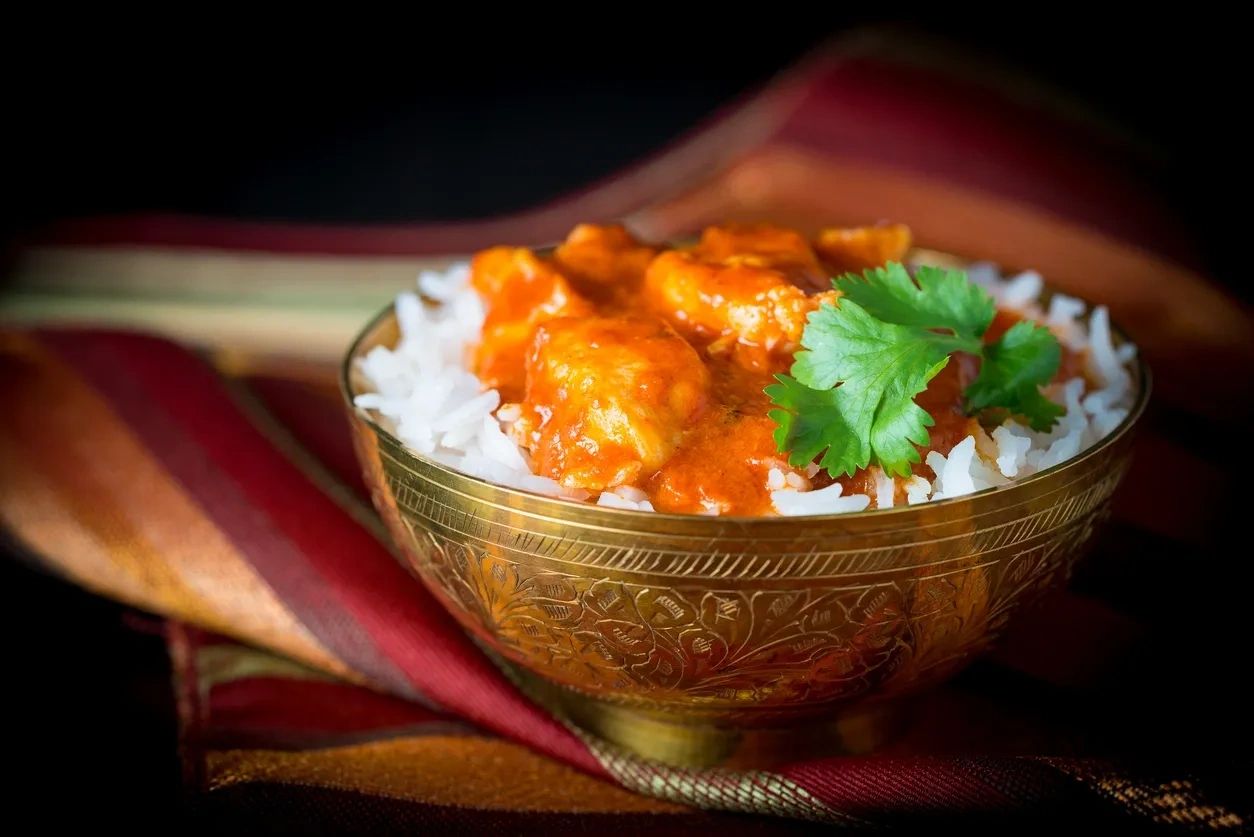 A bowl of creamy butter chicken served over white rice with a cilantro garnish.