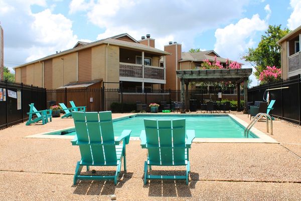 A serene outdoor pool area with turquoise chairs and apartment buildings.