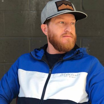 Man with a red beard wearing a blue and white jacket and gray cap.