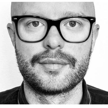 Close-up black and white portrait of a bald man with glasses and a beard.