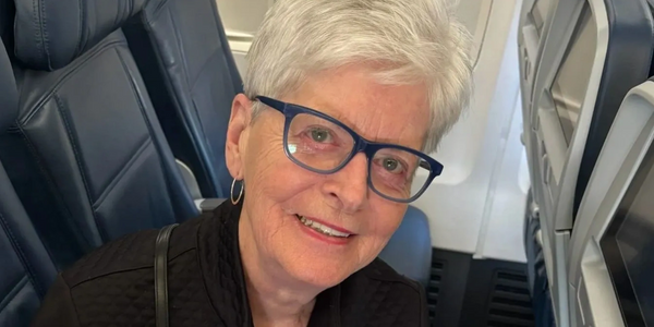 Elderly woman with white hair and glasses smiling on an airplane.
