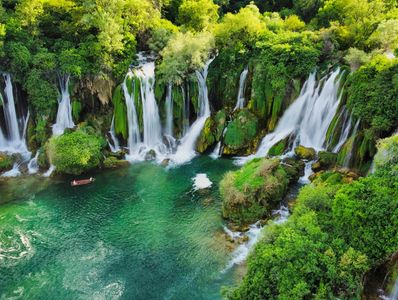 A lush green landscape with multiple cascading waterfalls and two boats on a clear river.