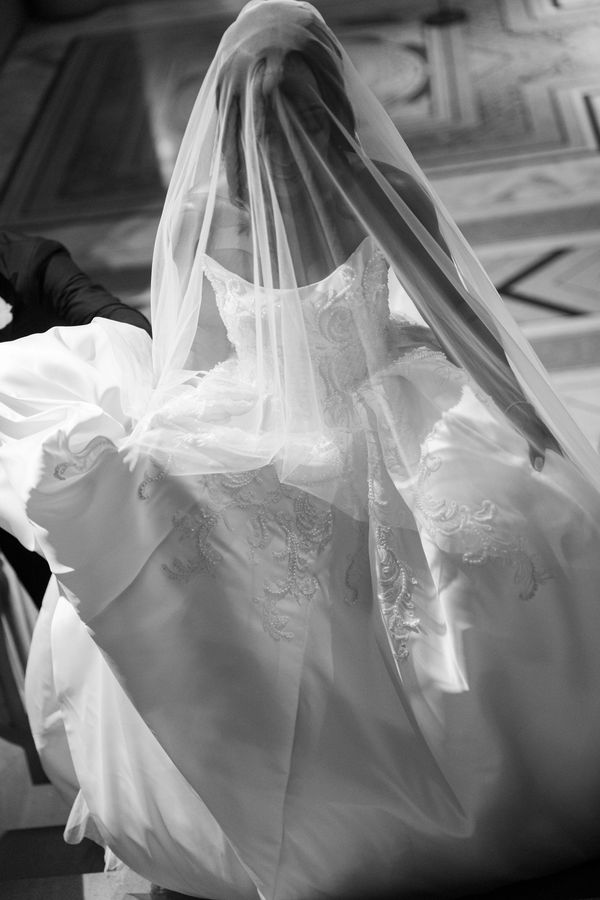 Black and white photo of a bride lifting her wedding dress and veil.