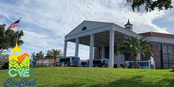 Community center with buses and palm trees under a partly cloudy sky.