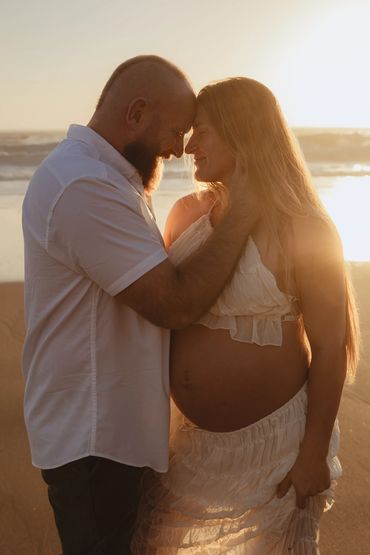 Pregnant couple sharing a tender moment at sunset.