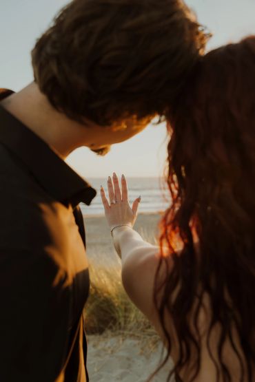 Couple admiring a ring on the beach at sunset.