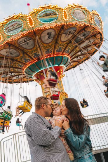 Parents kiss their baby at a carnival swing ride.