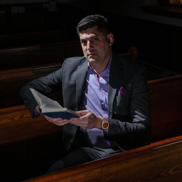 The Reverend Dr. Daniel Rodriguez Schlorff reads from a hymnal in a darkened church