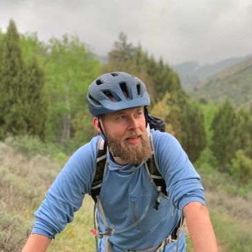 Bearded man in a blue helmet cycling outdoors in a natural setting.