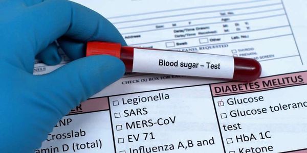 Gloved hand holding blood sugar test tube over a medical test form.