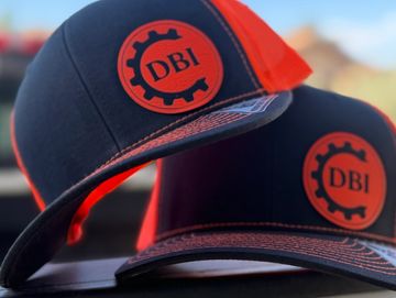 Two black and orange DBI hats stacked with gear logo.