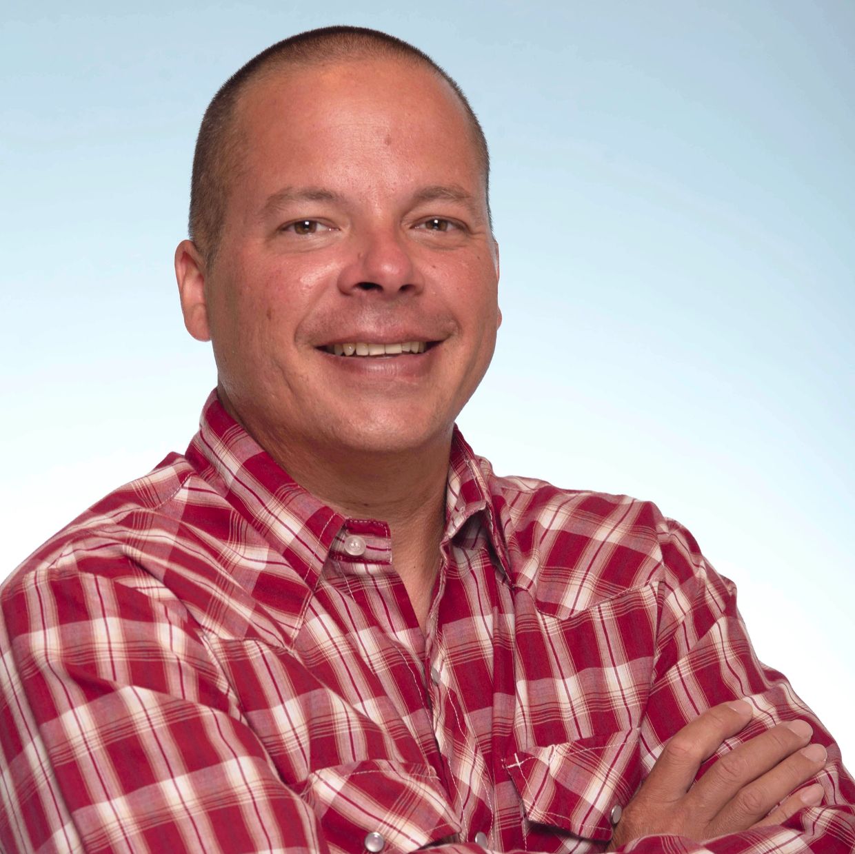 Smiling man in a red plaid shirt with crossed arms.