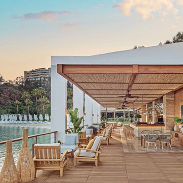 Elegant outdoor seating area by the water with wooden furniture and a shaded canopy.