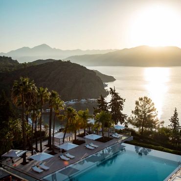Sunset view over a serene pool with mountains and sea in the background.