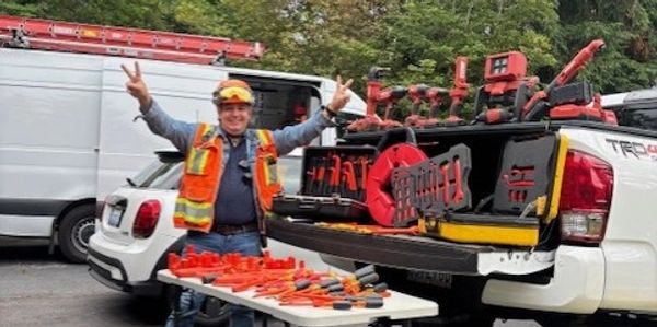 Worker in safety gear with tools displayed on a table and truck bed outdoors.