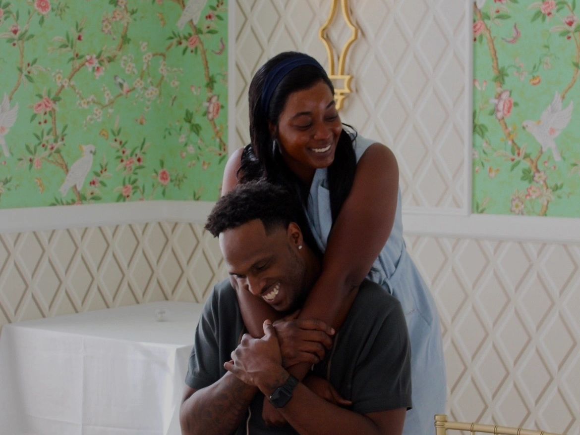 A joyful couple sharing a warm embrace indoors with floral wallpaper.