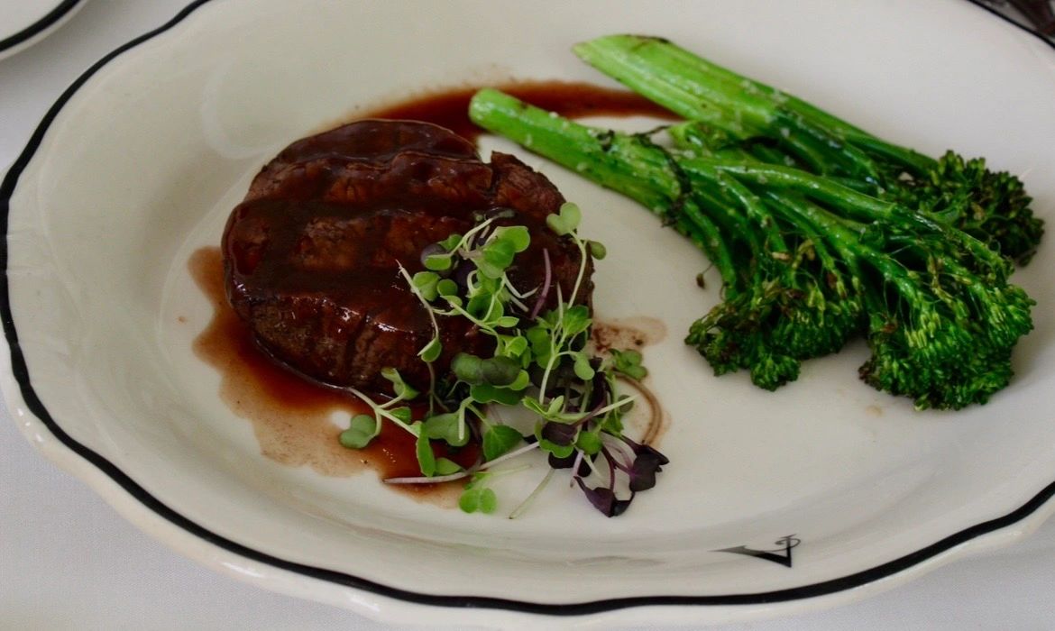 Grilled steak with sauce, microgreens, and broccolini on a white plate.