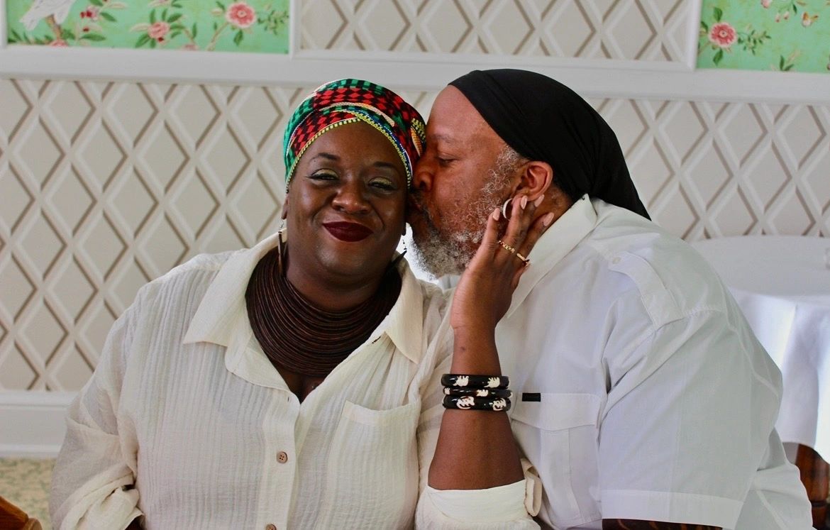 Man kisses woman on cheek, both smiling warmly indoors.