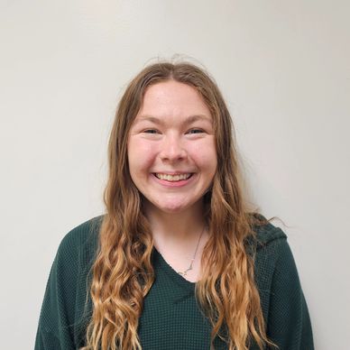 Smiling young woman with long wavy hair in a green sweater.