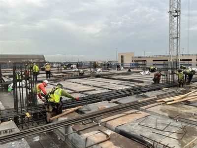 Construction workers installing rebar on a building site under cloudy skies.