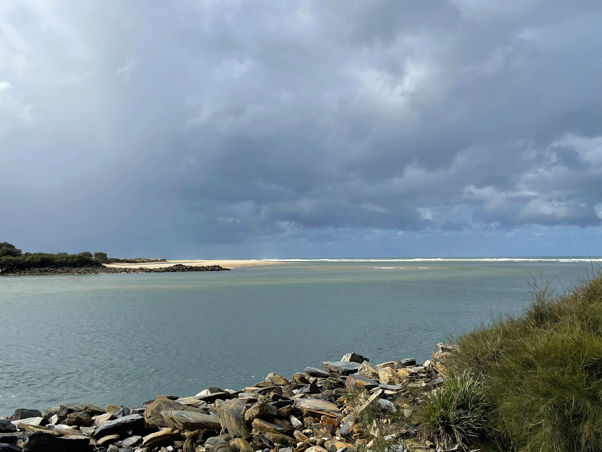 Cloudy sky over a rocky shoreline and calm sea.
