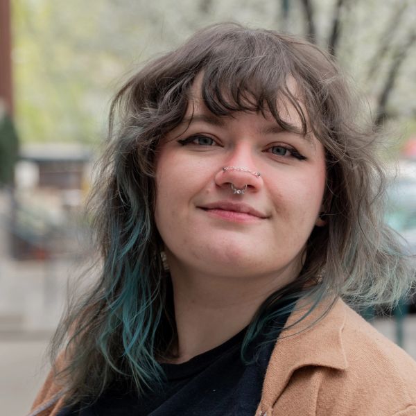 Portrait of a smiling young woman with blue-tinted hair and facial piercings.