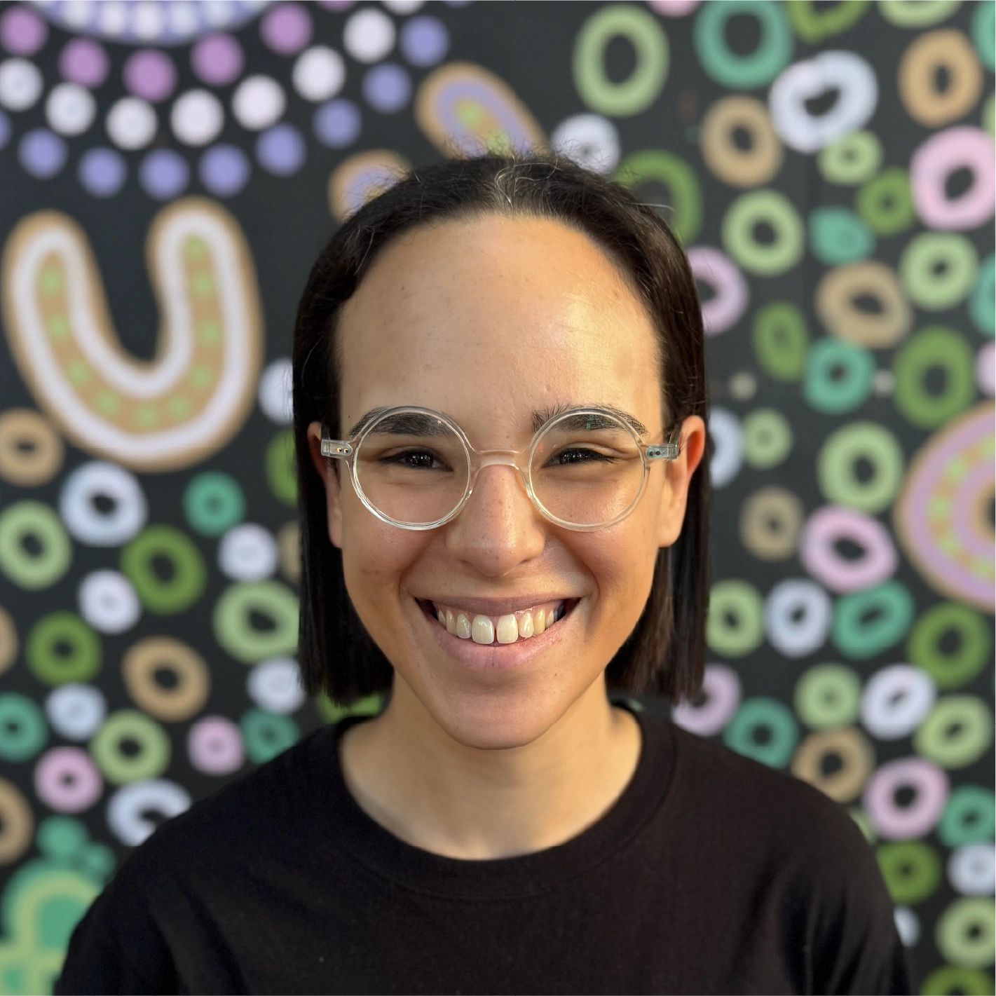 Smiling person with round glasses and colorful background.