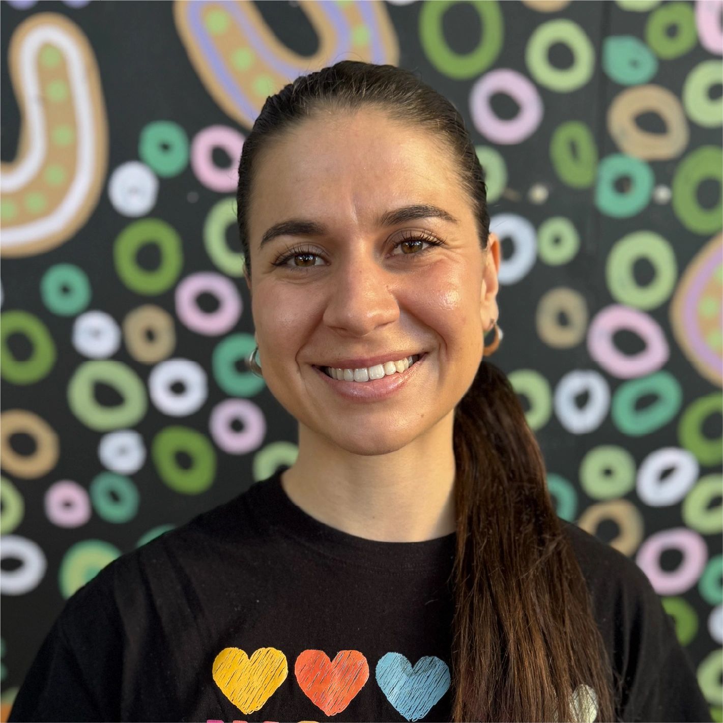 Smiling woman with long hair in front of colorful circular patterned wall.