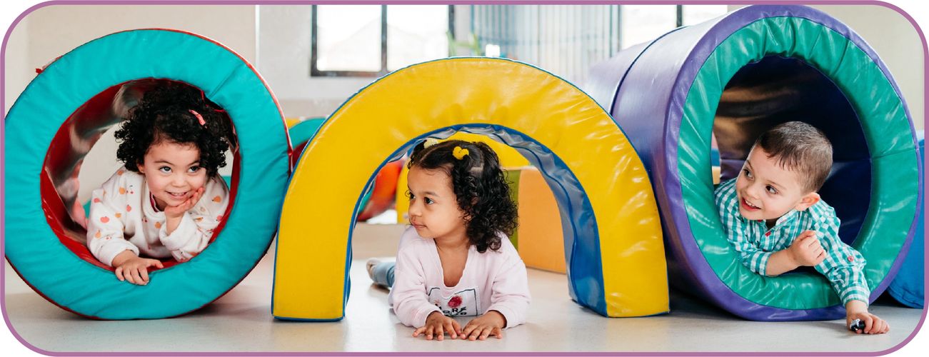 Three children hiding and playing with soft play equipment in an inclusive education setting. 