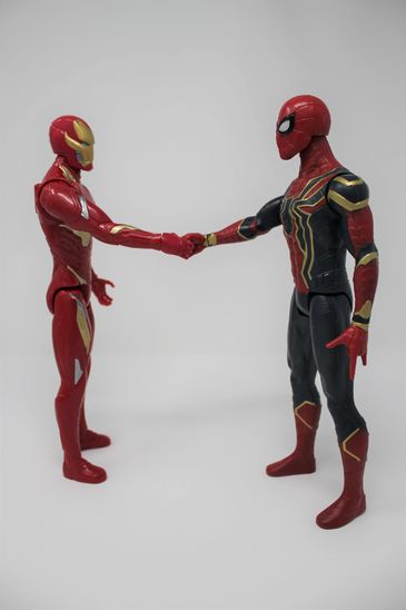 Spiderman and Ironman toys shaking hands.