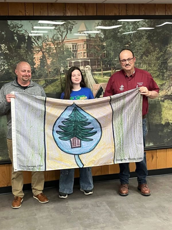 Three people holding a handmade flag with a tree design in front of a mural.
