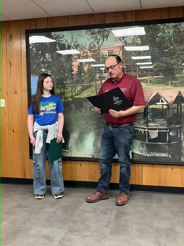 A man presents an award to a young girl in front of a mural.