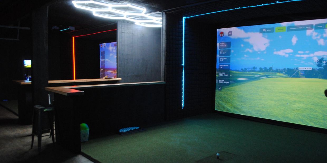 Indoor golf simulators with neon lighting and digital screens.