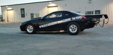 Black sports car with racing decals parked outside a garage at dusk.