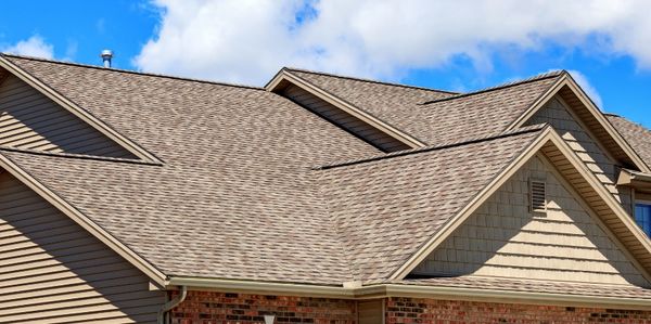 A residential house roof with asphalt shingles under a partly cloudy sky.
