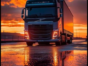 A Volvo truck is parked on a wet road reflecting the sunset colors.