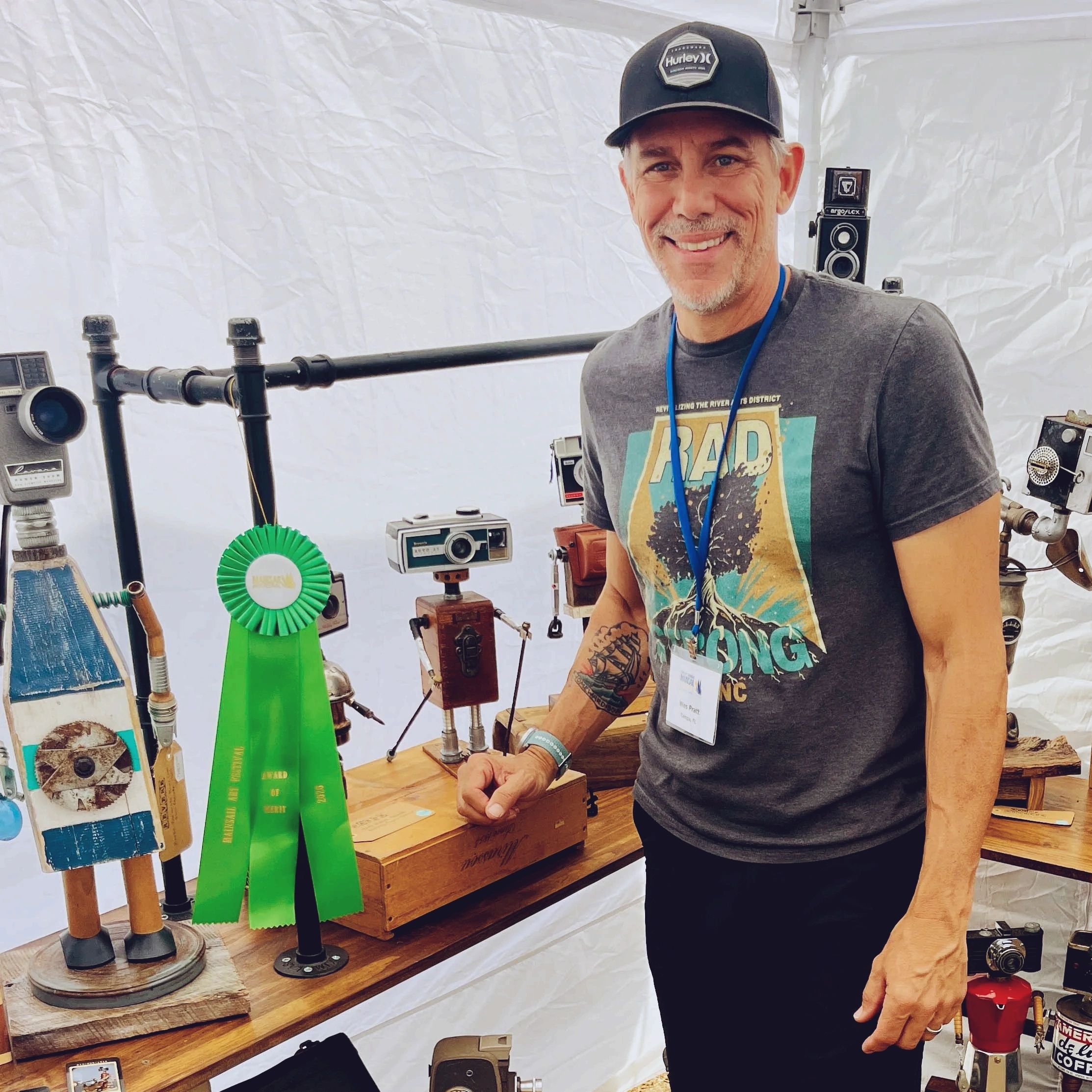 Man smiling with vintage camera robots and a green award ribbon.