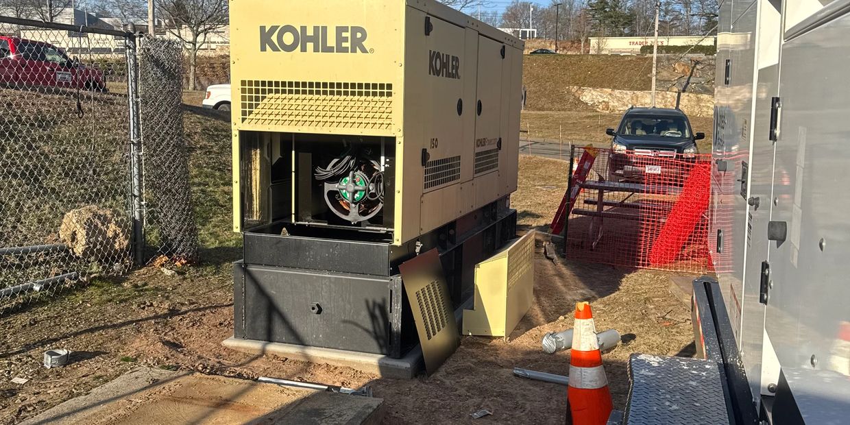 An open Kohler generator at a construction site with orange cones and fencing.