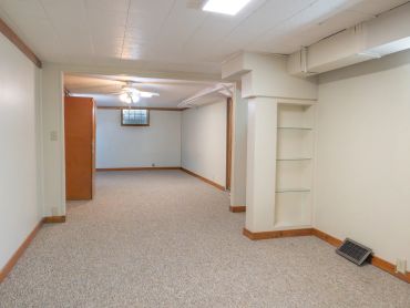 Empty basement room with beige carpet and white walls.